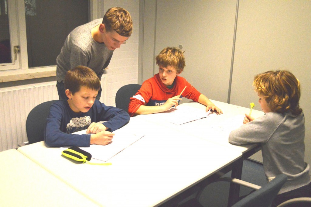 Nick Manshanden helpt de Stap 3-jeugdspelers Yannick, Sem en Lex bij het maken van hun huiswerk.
