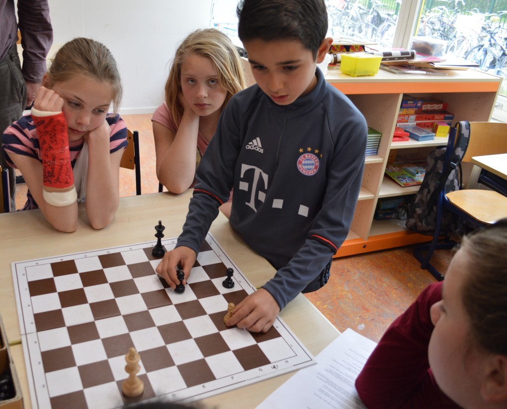 Een heel jonge 'schaaktrainer' legt uit hoe het werkt. De pion in zijn rechterhand moet de witte pion weglokken, waardoor de andere pion zal promoveren.